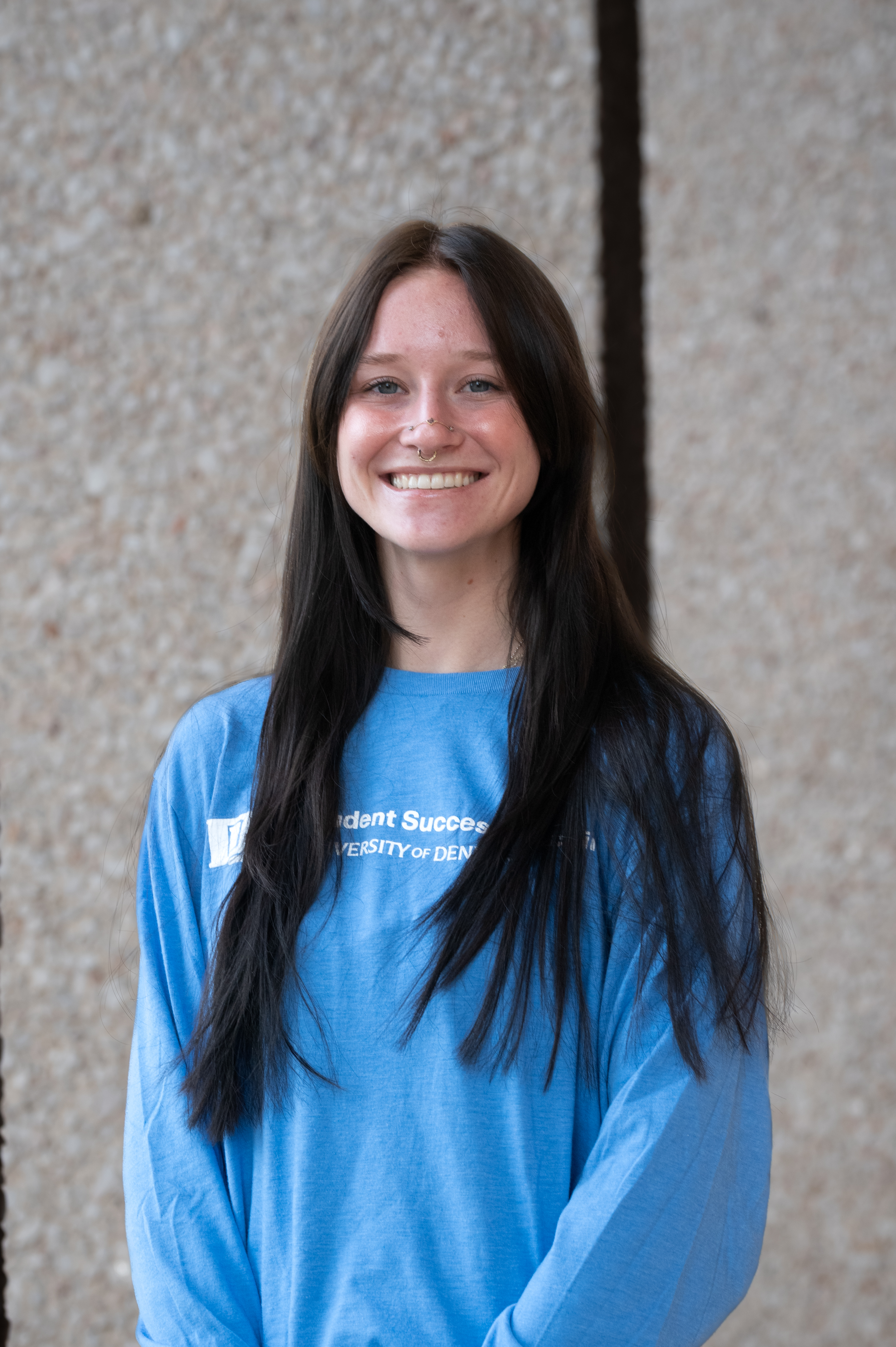 a female with long brown hair looking into the camera. Wearing a blue shirt with Student Success Coaching as the logo on the front.