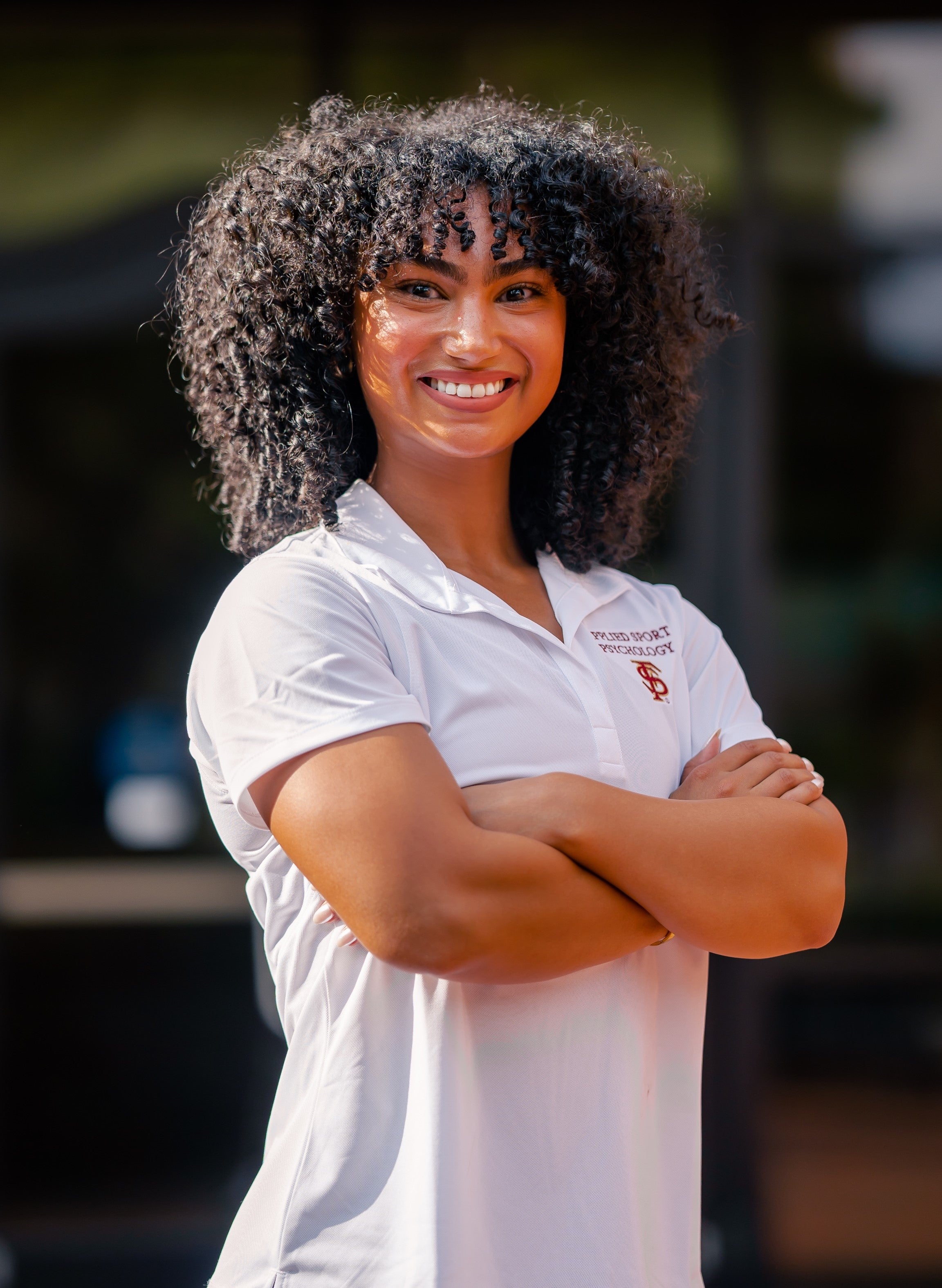 A female presenting woman wearing a white shirt looking into the camera smiling. She has black hair.