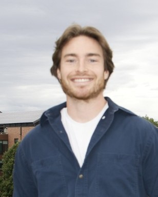 A white presenting male with short brown hair is smiling into a camera.