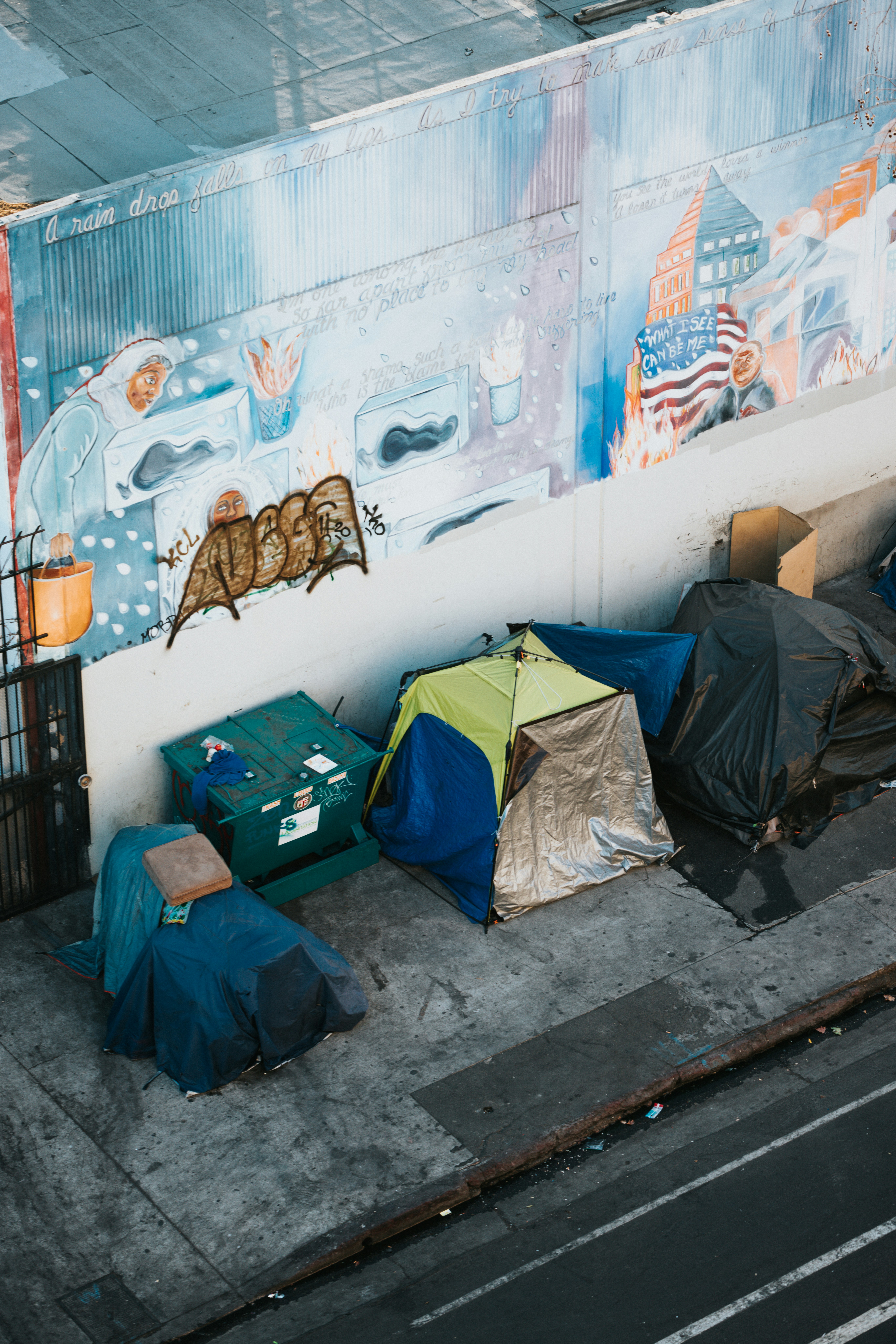 aerial view of three tents backed against a concrete wall with graffiti