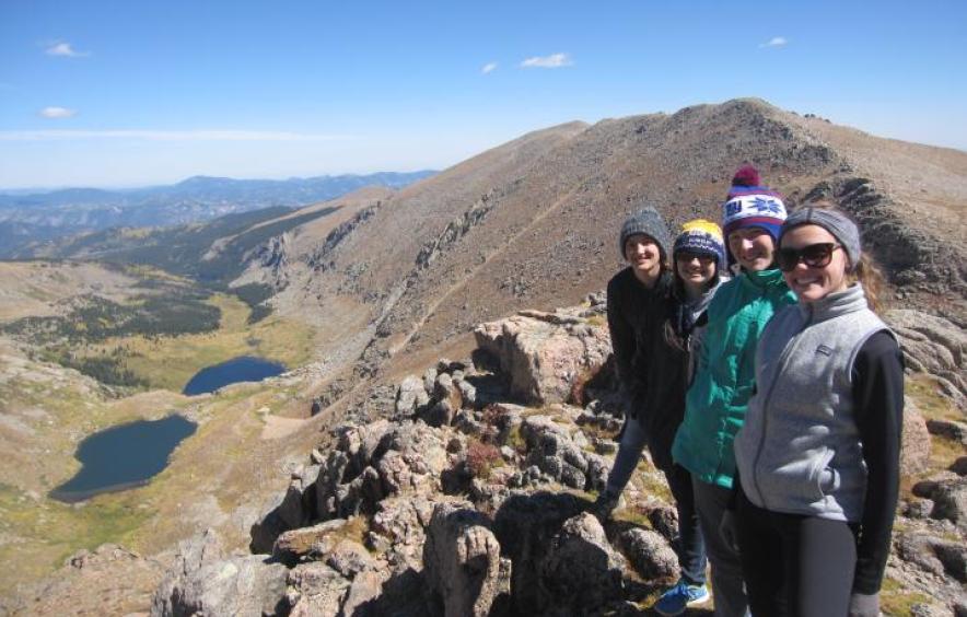 Four female-presenting students standing on top of a mountain together