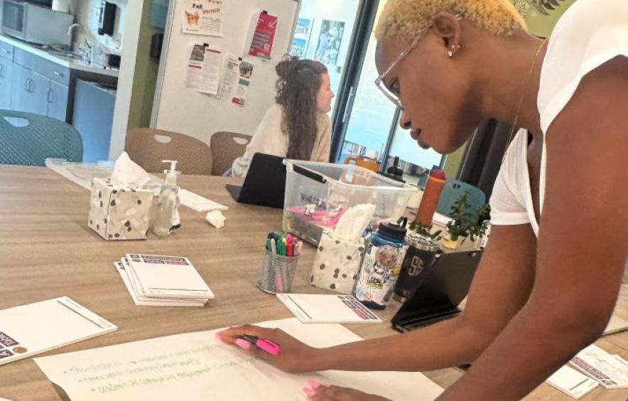 group of students bent over table writing on large paper pieces