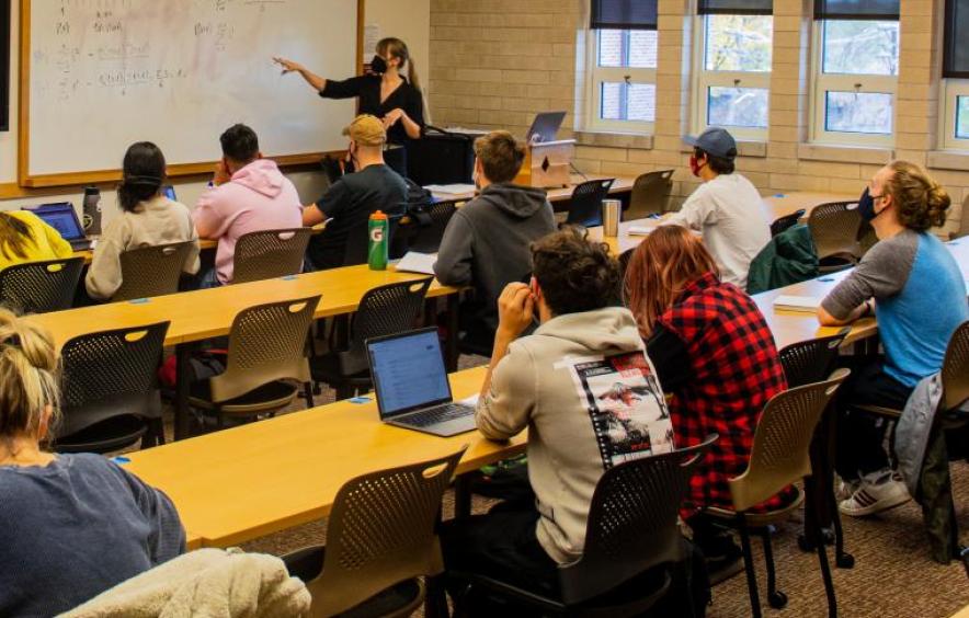 Professor in classroom pointing to a whiteboard with math figures