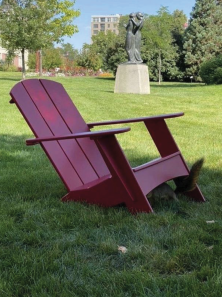 A University of Denver red Adirondack chair with a squirrel under it.