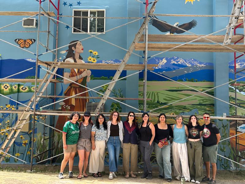 group of people standing in front of scaffolding and a mural