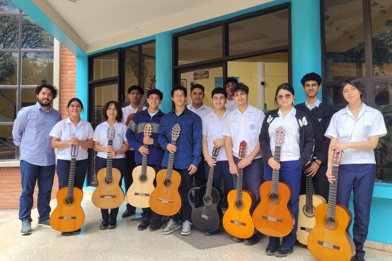 group of students holding guitars and lined up in front of building