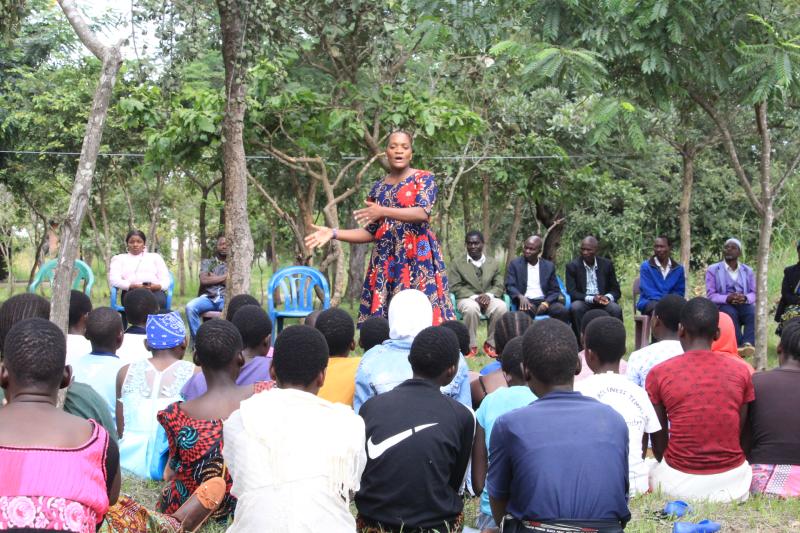 group of people sitting amid trees listening to a speaker