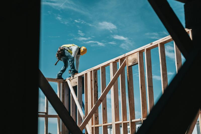 A construction worker stands atop the house's framework, building.