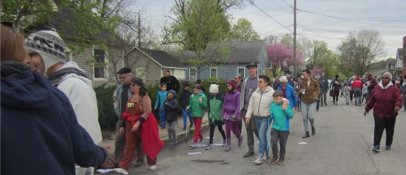 group of people walking down the treelined street with houses on one side