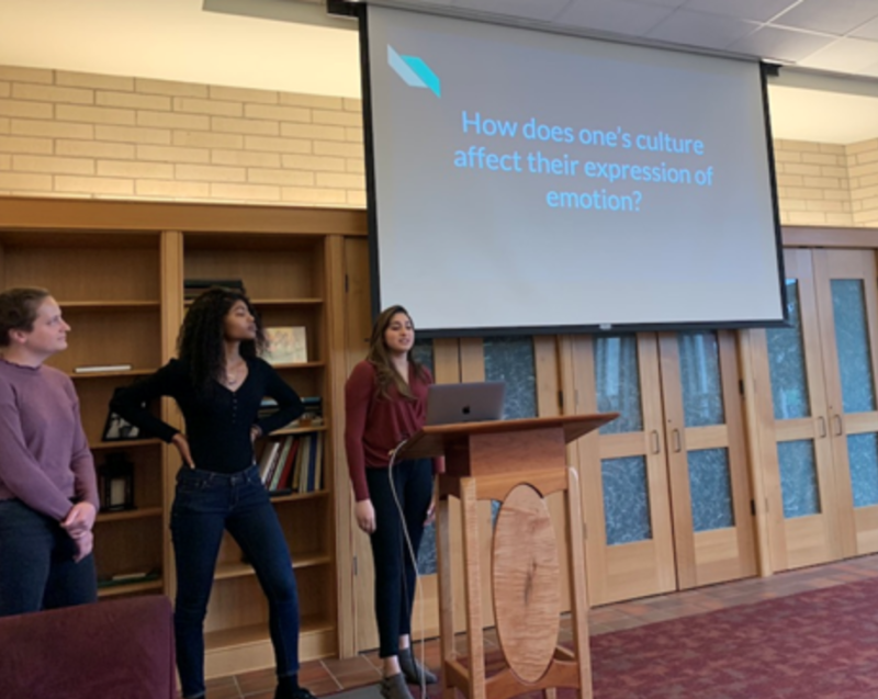 three students presenting in front of a screen