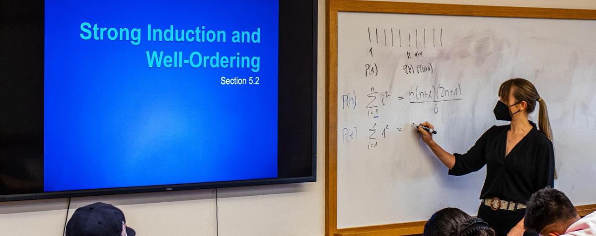 Professor writes on a whiteboard in front of the class
