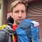 David H: A photo of David wearing two backpacks and a rain jacket while hiking the Camino de Santiago.