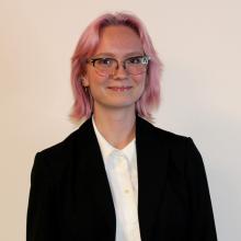 Woman with pink hair and glasses smiles at camera