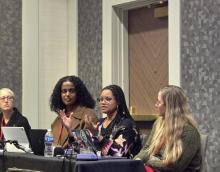 two women sitting at conference table speaking to crowd