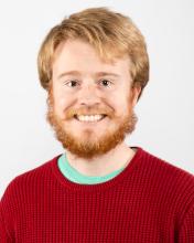 Hunter has short, red hair and a red beard. He smiles while wearing a red sweater.
