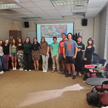 A professor at the University of Denver stands with students in their classroom following a presentation