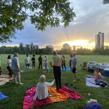 A group standing in a circle, in a park at sunset
