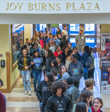 Students walking through building with sign reading "Joy Burns Plaza" overhead